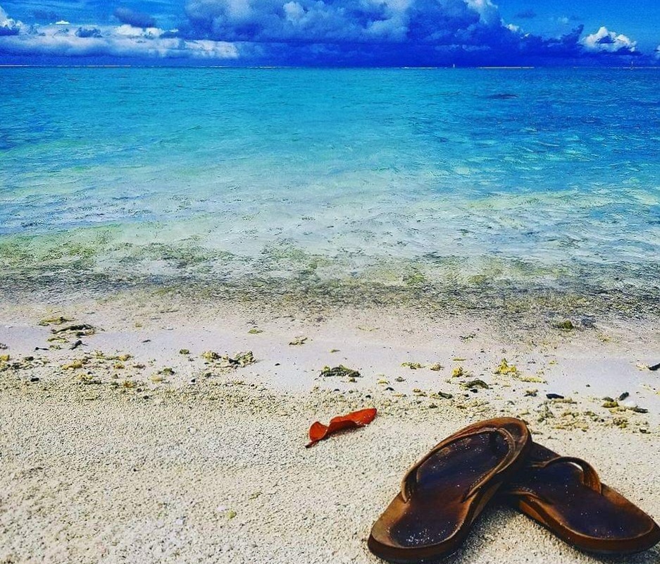 Flip flops on a white sand beach with clear blue ocean.